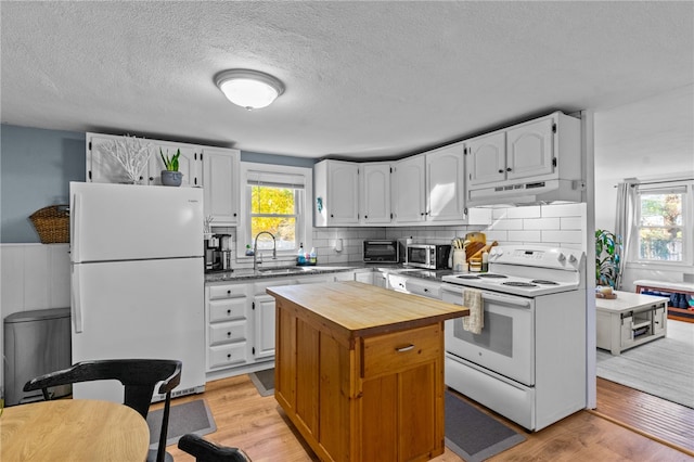 kitchen with a wealth of natural light, white cabinets, light hardwood / wood-style floors, and white appliances