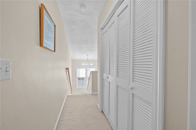 hallway with light carpet and an inviting chandelier