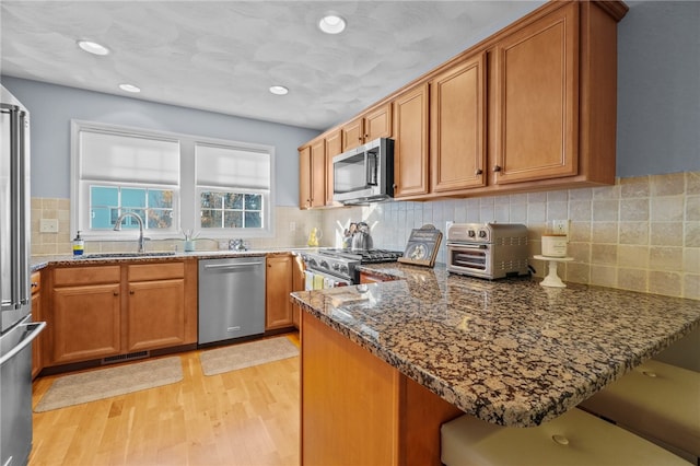 kitchen with dark stone counters, sink, light hardwood / wood-style flooring, kitchen peninsula, and stainless steel appliances