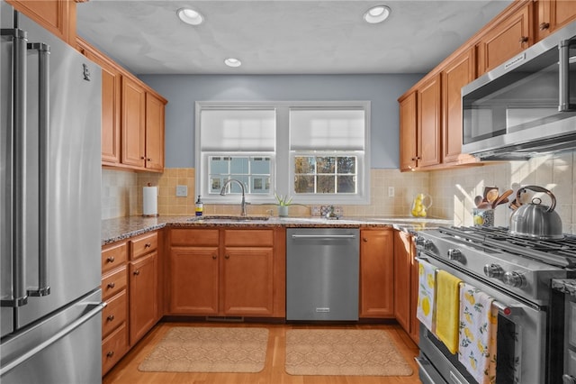 kitchen with sink, light stone countertops, tasteful backsplash, premium appliances, and light hardwood / wood-style floors