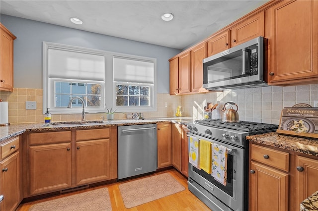 kitchen with light stone countertops, sink, stainless steel appliances, and light wood-type flooring