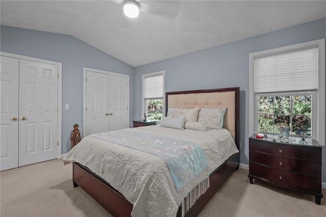 bedroom featuring ceiling fan, light colored carpet, lofted ceiling, and two closets