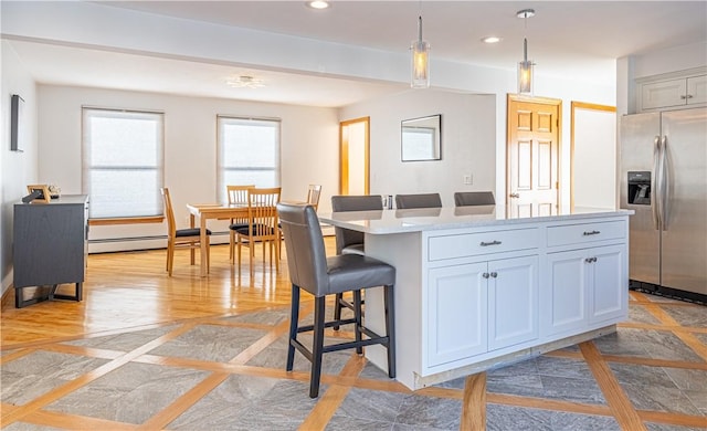 kitchen with a center island, hanging light fixtures, stainless steel fridge with ice dispenser, a baseboard heating unit, and a kitchen bar