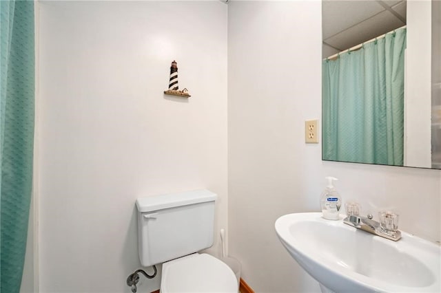 bathroom featuring a drop ceiling, toilet, curtained shower, and sink