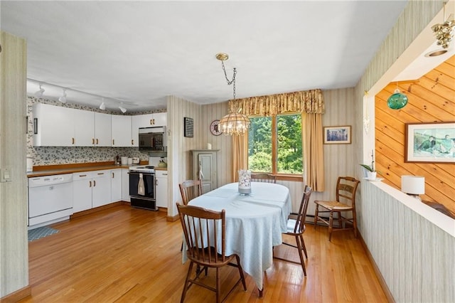 dining area featuring a chandelier, rail lighting, light hardwood / wood-style flooring, and wood walls