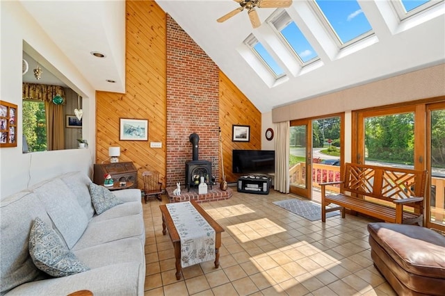 living room with high vaulted ceiling, a wood stove, a healthy amount of sunlight, and light tile patterned flooring