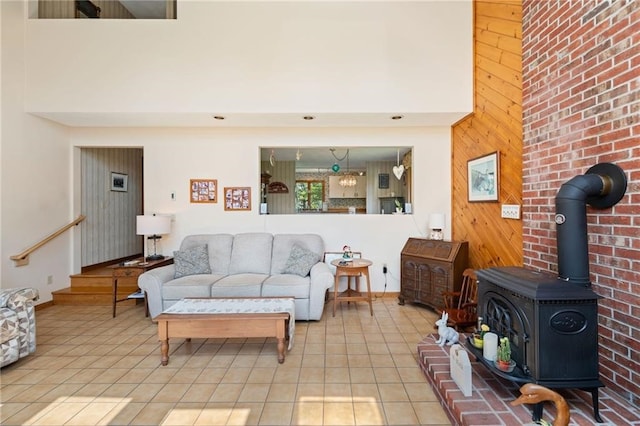 living room with a wood stove, wooden walls, a towering ceiling, and light tile patterned floors