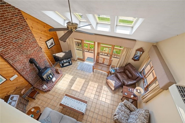 living room with a wood stove, wood walls, ceiling fan, and a skylight