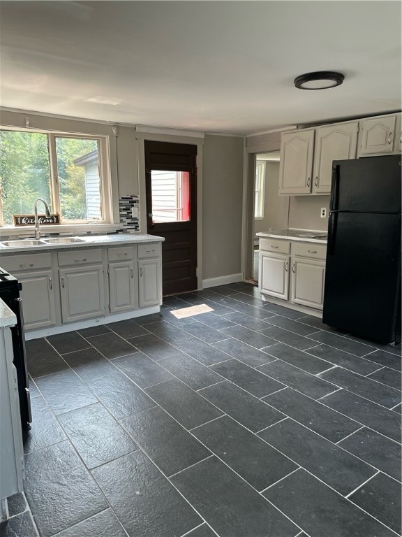 kitchen featuring white cabinetry, black fridge, and sink