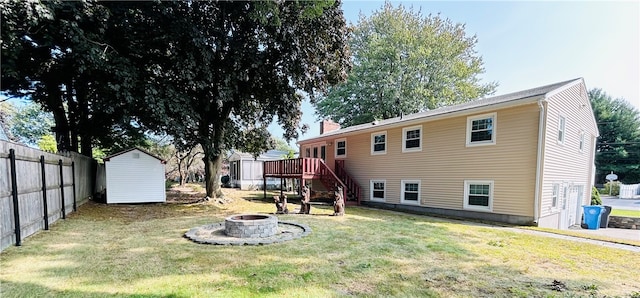 rear view of house with a shed, a fire pit, a wooden deck, and a lawn