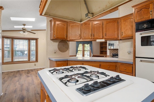 kitchen featuring ceiling fan, lofted ceiling with skylight, crown molding, wood-type flooring, and white appliances