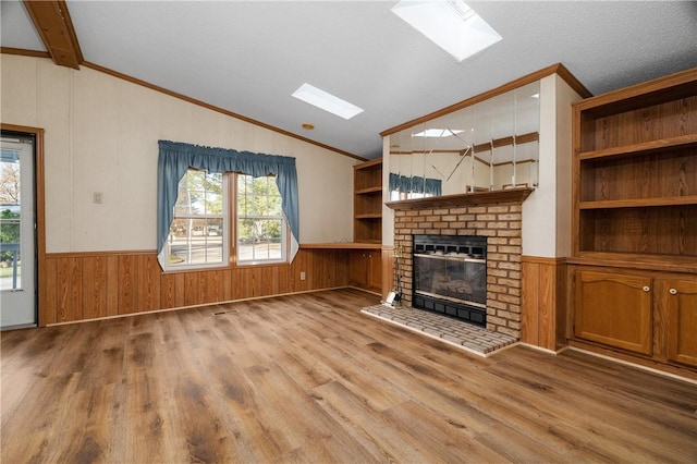 unfurnished living room with crown molding, light hardwood / wood-style flooring, vaulted ceiling with skylight, a fireplace, and a textured ceiling