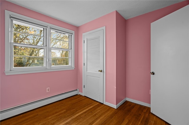 unfurnished bedroom featuring dark wood-type flooring, a closet, and a baseboard heating unit