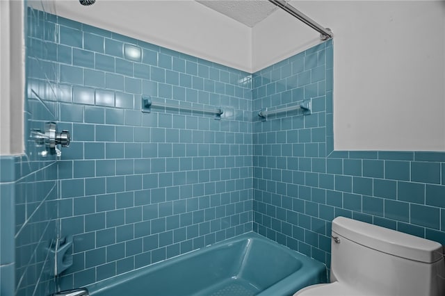 bathroom with a textured ceiling, tiled shower / bath combo, toilet, and tile walls