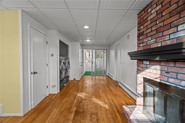 doorway with a brick fireplace, light hardwood / wood-style floors, washing machine and dryer, and a baseboard heating unit