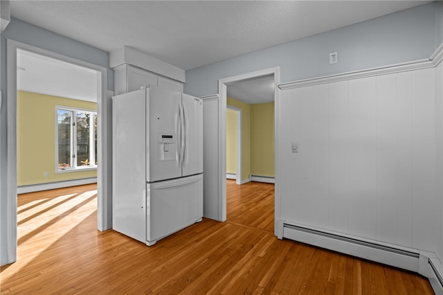 kitchen featuring white refrigerator with ice dispenser, light wood-type flooring, a baseboard radiator, and white cabinetry