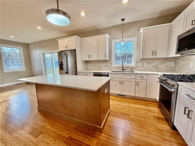 kitchen featuring decorative light fixtures, high quality appliances, sink, white cabinets, and a center island