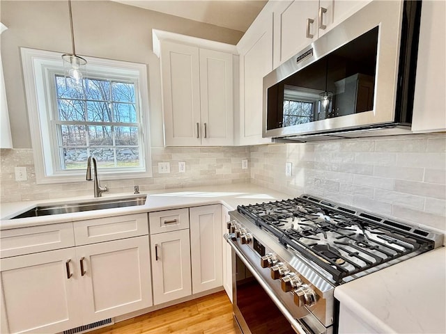 kitchen with pendant lighting, sink, stainless steel appliances, light hardwood / wood-style floors, and white cabinets