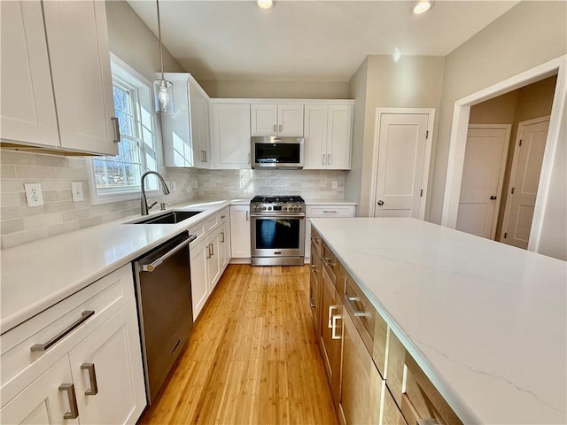 kitchen with sink, stainless steel appliances, light stone counters, white cabinets, and decorative light fixtures