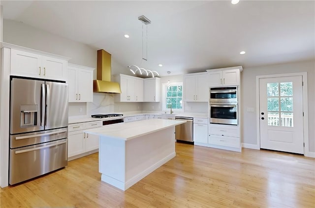 kitchen featuring wall chimney exhaust hood, a center island, pendant lighting, stainless steel appliances, and white cabinets