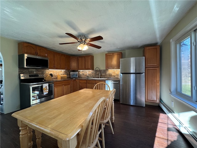 kitchen featuring decorative backsplash, appliances with stainless steel finishes, dark hardwood / wood-style flooring, sink, and a baseboard radiator