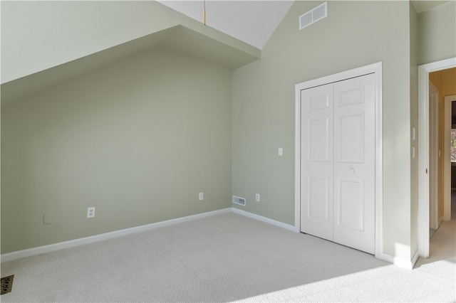 unfurnished bedroom featuring a closet, high vaulted ceiling, and light colored carpet