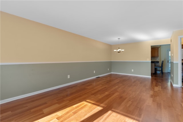 empty room with hardwood / wood-style floors and a notable chandelier