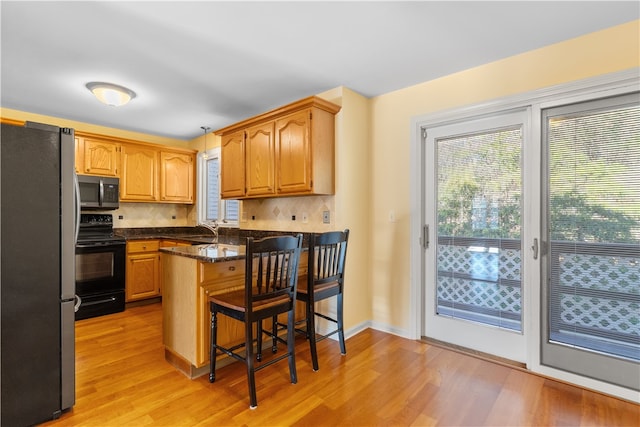 kitchen with kitchen peninsula, a breakfast bar, stainless steel appliances, and light hardwood / wood-style floors