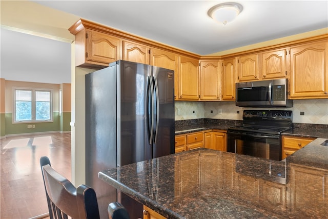 kitchen with dark stone countertops, kitchen peninsula, appliances with stainless steel finishes, and tasteful backsplash