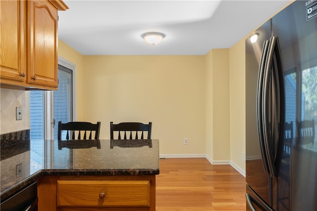 kitchen with decorative backsplash, refrigerator, dark stone countertops, and light hardwood / wood-style floors