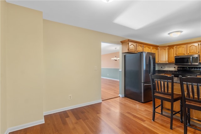 kitchen with a notable chandelier, light hardwood / wood-style floors, backsplash, and appliances with stainless steel finishes