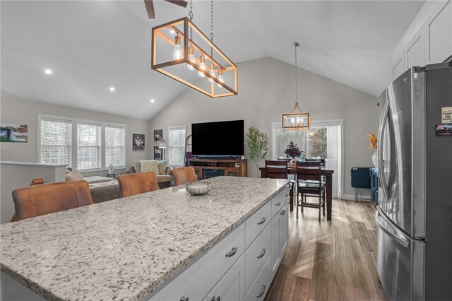 kitchen with stainless steel fridge, light stone counters, pendant lighting, white cabinetry, and a kitchen island