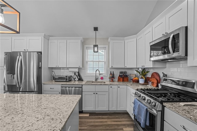 kitchen with lofted ceiling, white cabinets, sink, appliances with stainless steel finishes, and decorative light fixtures