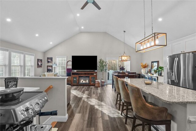 interior space featuring pendant lighting, a breakfast bar, white cabinets, stainless steel fridge, and light stone countertops