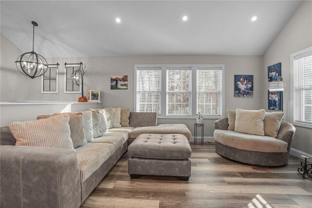 living room with hardwood / wood-style flooring, an inviting chandelier, and vaulted ceiling