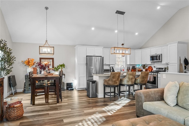 interior space with stainless steel appliances, pendant lighting, a kitchen bar, decorative backsplash, and white cabinets