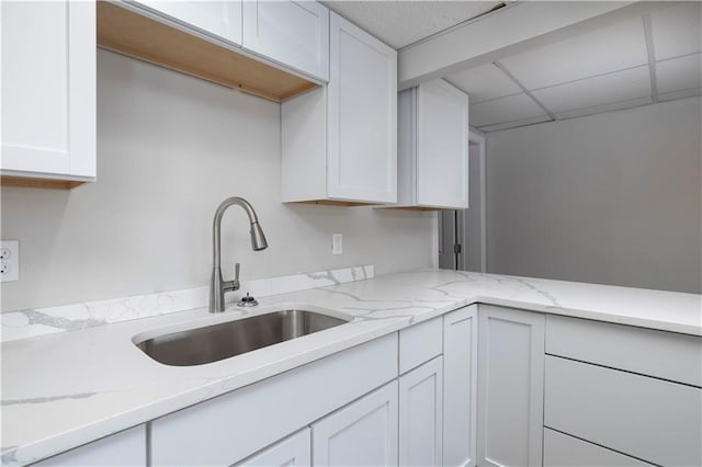 kitchen with light stone counters, sink, white cabinets, and a drop ceiling