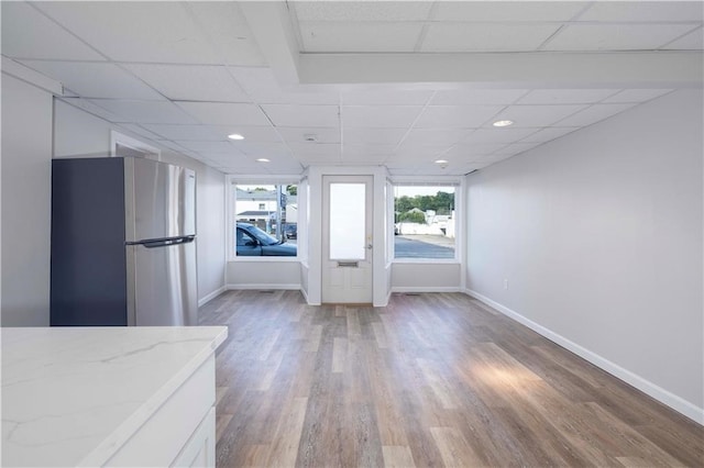 kitchen featuring a paneled ceiling, light stone countertops, wood-type flooring, and stainless steel refrigerator