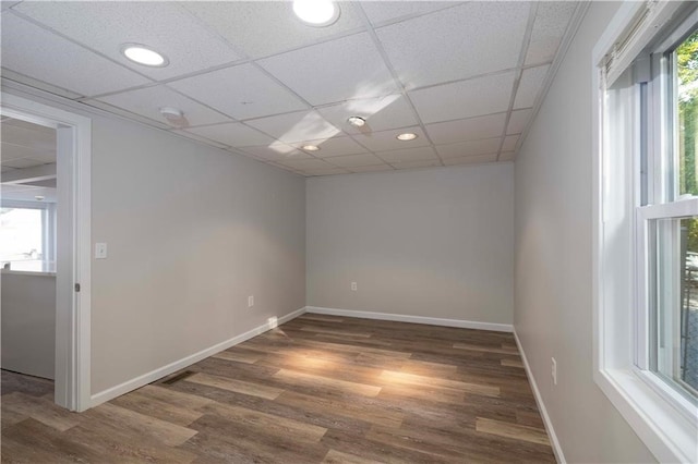 empty room with a paneled ceiling, a healthy amount of sunlight, and dark hardwood / wood-style flooring