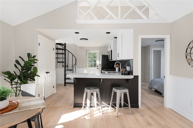 kitchen with kitchen peninsula, vaulted ceiling, white cabinetry, and a breakfast bar area