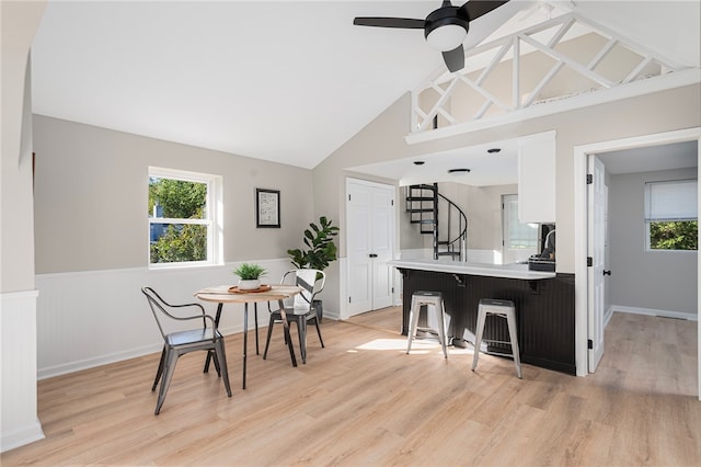 kitchen featuring kitchen peninsula, a kitchen breakfast bar, high vaulted ceiling, light hardwood / wood-style floors, and white cabinetry