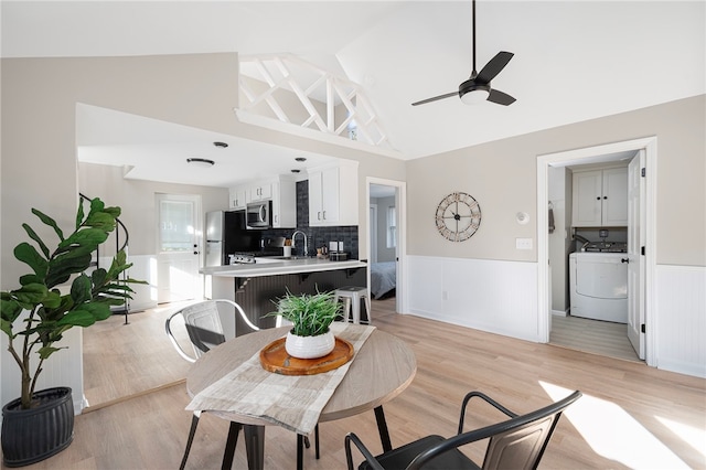 dining area featuring ceiling fan, sink, high vaulted ceiling, washer / dryer, and light hardwood / wood-style floors