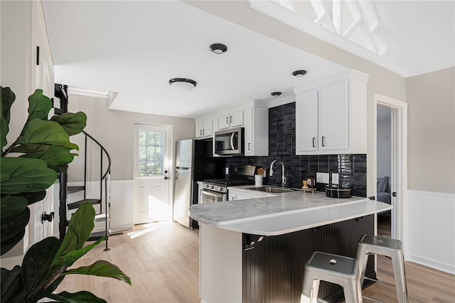 kitchen featuring white cabinetry, sink, stainless steel appliances, kitchen peninsula, and a breakfast bar