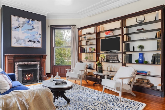 living area with a fireplace, wood-type flooring, and ornamental molding