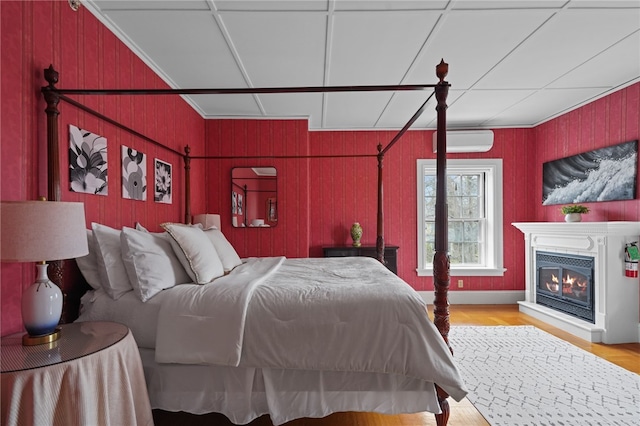 bedroom featuring a wall mounted air conditioner, wooden walls, light hardwood / wood-style flooring, and ornamental molding