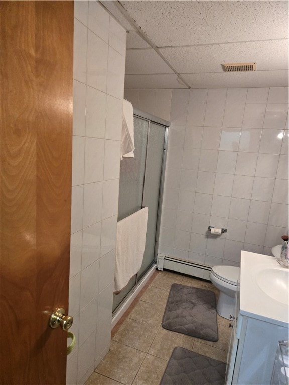 bathroom with a drop ceiling, baseboard heating, tile patterned flooring, a shower with door, and vanity