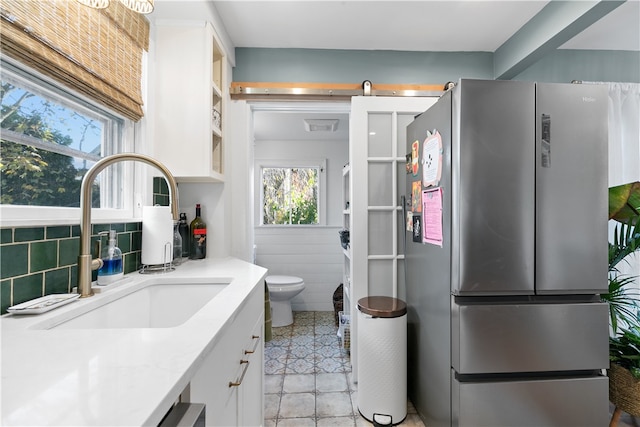 kitchen with backsplash, sink, light tile patterned floors, white cabinets, and stainless steel refrigerator