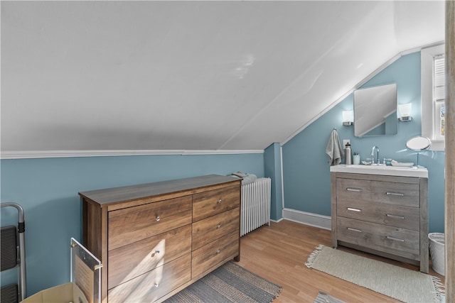 bedroom featuring light hardwood / wood-style floors, radiator, lofted ceiling, and sink