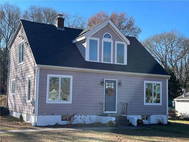 new england style home featuring a shingled roof, a front yard, and a chimney