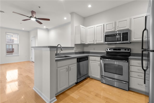 kitchen with appliances with stainless steel finishes, sink, light wood-type flooring, and kitchen peninsula